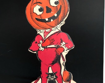 May include: A vintage Halloween cutout of a pumpkin-headed figure in a red suit, holding a black cat. The figure has a wide grin and large eyes. The cutout is printed on cardstock and has a black border.