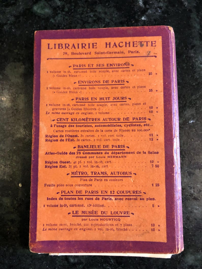 May include: A vintage red and orange book cover with the title "Librairie Hachette" and a list of books and prices in French. The book is about Paris and its surrounding areas.