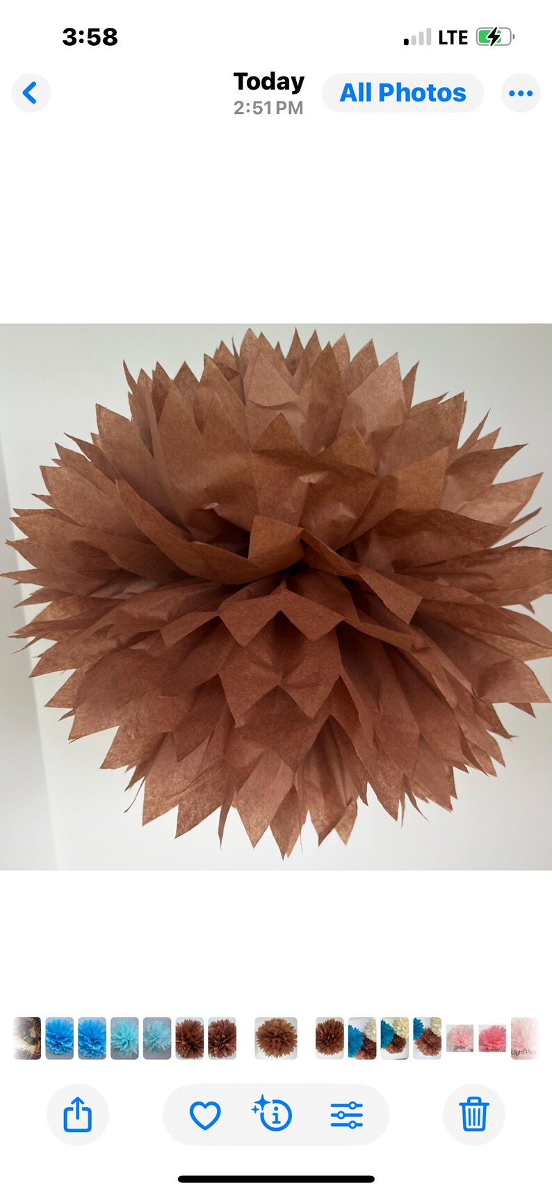 May include: A spherical paper pom-pom decoration in a solid brown color. The object is constructed from multiple layers of thin, translucent paper sheets with pointed, jagged edges that fan out to create a full, textured, and voluminous floral shape.