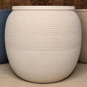 May include: Three round planters with a smooth base and a textured upper section featuring horizontal ridges. The planters are colored in dark blue, off-white, and light brown. Each container has a wide opening and a rounded, bulbous body shape.