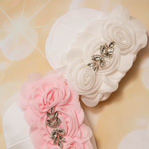 May include: Two white fabric baby hats with pink and white fabric flowers and rhinestone embellishments.