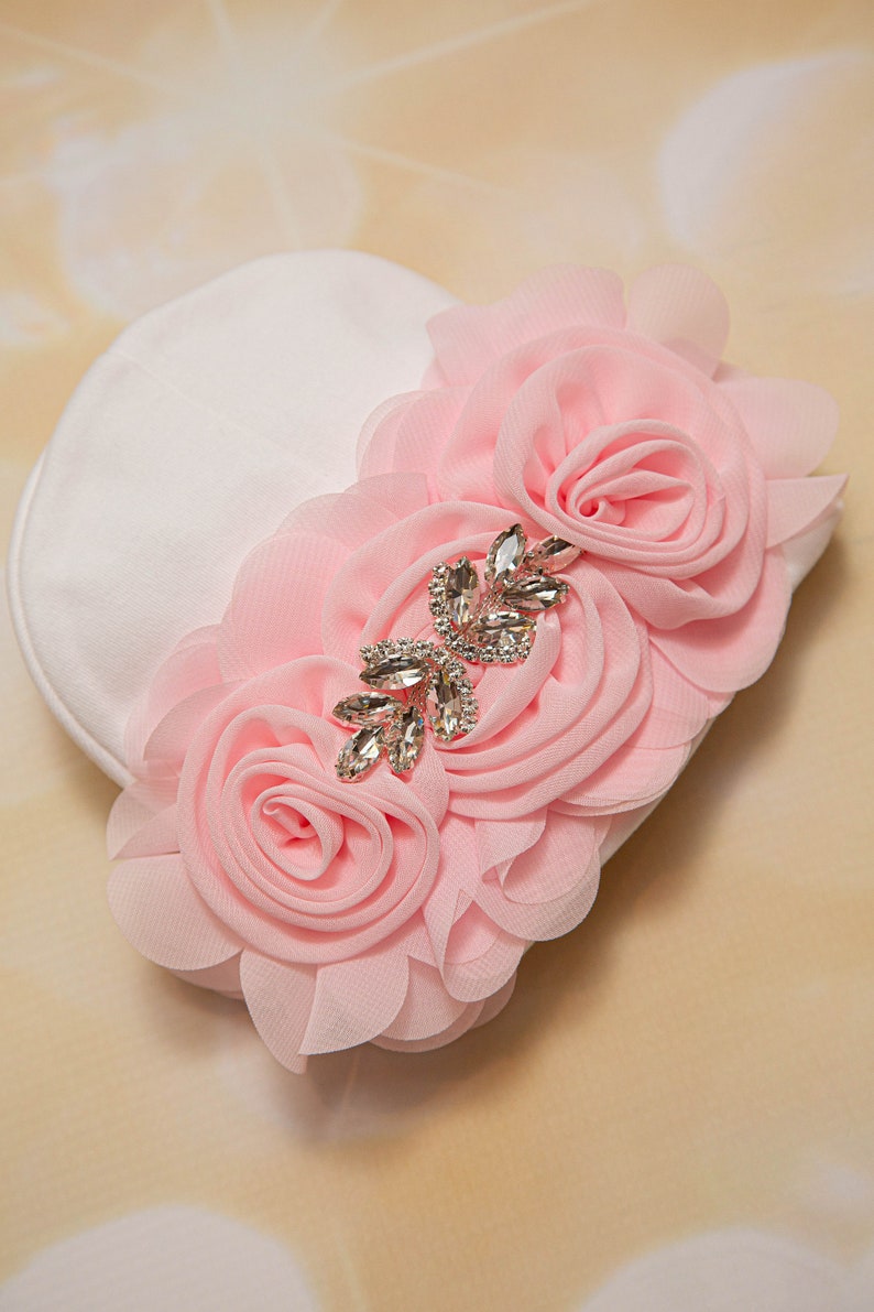 May include: A white fabric headband with three pink fabric roses and a rhinestone embellishment.