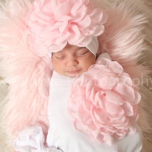 May include: A sleeping baby wearing a pink flower headband and a white onesie. The baby is lying on a pink fluffy surface.