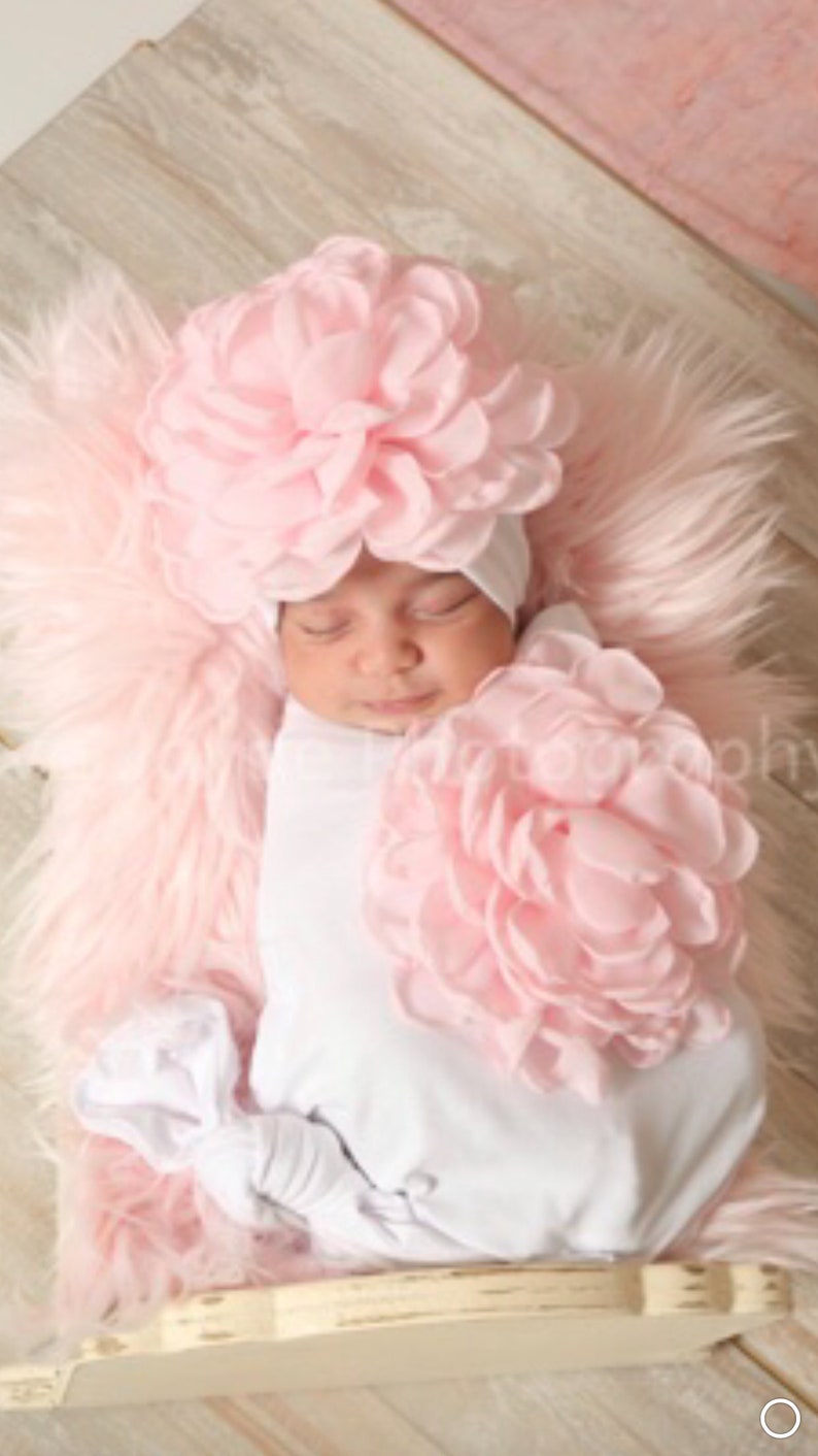 May include: A sleeping baby wearing a pink flower headband and a white onesie. The baby is lying on a pink fluffy surface.