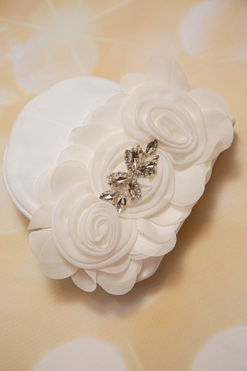 May include: White fabric headband with a large white flower and a rhinestone embellishment.