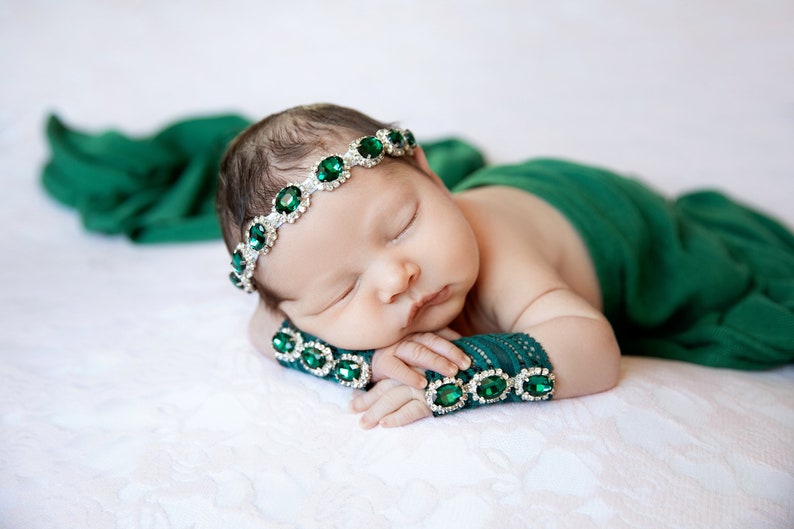 K&ouml;nnte beinhalten: Ein schlafendes Baby, das ein gr&uuml;nes Stirnband mit smaragdgr&uuml;nen Edelsteinen und passende gr&uuml;ne Armb&auml;nder mit smaragdgr&uuml;nen Edelsteinen tr&auml;gt.