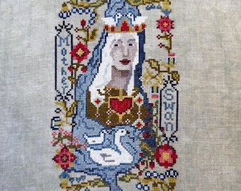 May include: A cross-stitch embroidery on light gray linen fabric featuring a central figure wearing a crown and blue cloak, with a red heart on the chest, a white swan, and the text "Mother" and "Swan" framed by floral motifs and crescent moons.