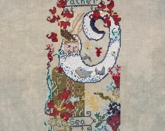 May include: A cross-stitch embroidery on light beige fabric featuring a crescent moon shape containing a face, surrounded by red coral, sea life, and anchors. The text "Father" appears at the top and "Sea" at the bottom in decorative banners.