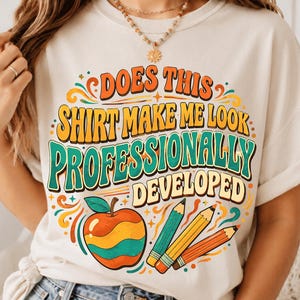 Könnte beinhalten: Ein cremefarbenes T-Shirt mit einem Aufdruck, der den Text "DOES THIS SHIRT MAKE ME LOOK PROFESSIONALLY DEVELOPED" in Orange, Gelb und Petrol zeigt. Das Design enthält einen stilisierten Apfel und drei Buntstifte in Petrol, Gelb und Orange.