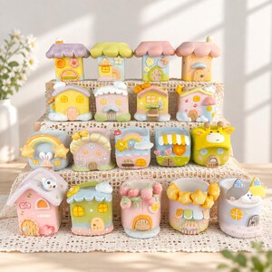 May include: A collection of small, colourful house-shaped planters and containers arranged on a tiered display. Each piece features pastel colours, whimsical architectural details like arched doors and windows, and decorative elements such as stars, rainbows, and fruit.