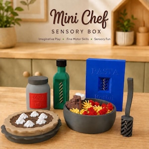 Op de afbeelding: Een Mini Chef Sensory Box set met een grijze pastasauspot met rood etiket, een groene fles, een blauwe doos met het opschrift Pasta Rotini, een grijze kom gevuld met gele en rode rotini pasta, een grijze pastaschep en een bruine taart met witte toefjes.