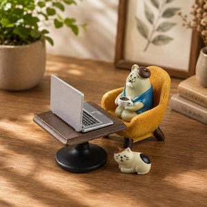 May include: A miniature figurine of a bear wearing a beret and blue shirt, sitting in a yellow armchair while holding a white coffee mug. A silver laptop sits on a small brown table, and a small white and black cat figurine rests on the floor.