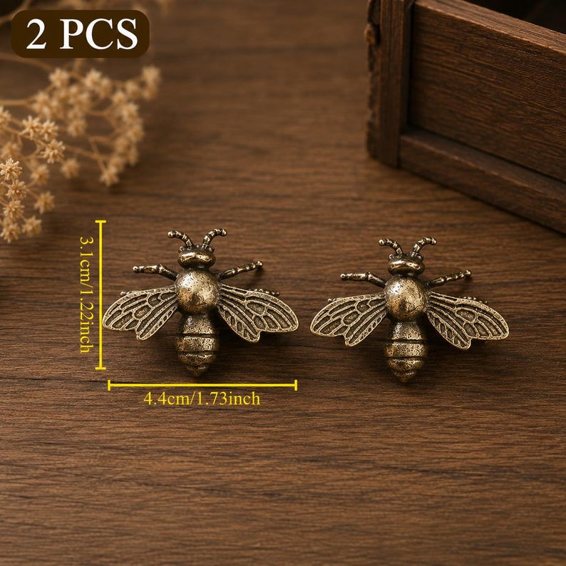 Peut inclure: Deux ornements en m&eacute;tal en forme d'abeille de couleur bronze antique. Chaque pi&egrave;ce pr&eacute;sente des ailes d&eacute;taill&eacute;es et un corps segment&eacute;. Le texte indique 2 PCS et des dimensions de 3,1 cm sur 4,4 cm. Les ornements ont une finition textur&eacute;e.