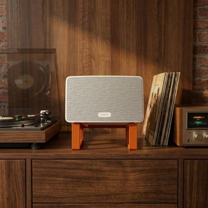 Può includere: Un altoparlante Sonos rettangolare bianco con una griglia frontale in rete, posizionato su un supporto arancione brillante. L'altoparlante presenta il logo Sonos centrato nella parte inferiore del pannello frontale, offrendo una vista chiara.