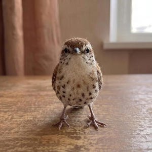 Puede incluir: Una pequeña figura de pájaro hecha a mano con un cuerpo texturizado de color marrón y crema. El pájaro presenta un patrón de pecho moteado, un pequeño pico puntiagudo y patas finas similares a alambres que sostienen su postura.