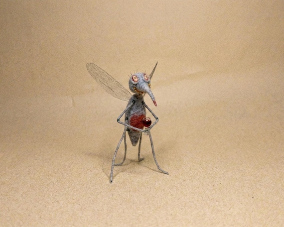 A needle-felted mosquito holding a tiny wine glass — hilariously specific, clearly handmade, and the kind of shelf piece that makes every guest do a double-take.