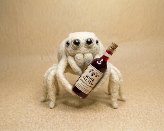 A handmade white wool spider hugging a miniature wine bottle — the kind of hyper-specific oddity that only a real crafts person dreams up.