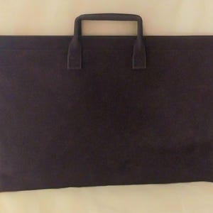 May include: A rectangular dark brown portfolio case with a flat, smooth surface and a single top-mounted handle. The case features a clean, minimalist design with a horizontal seam running across the upper portion, providing a structured appearance.
