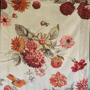 May include: A rectangular fabric panel featuring a beige background with a floral pattern of dahlias in shades of orange, deep red, and soft pink. The design includes green and gray foliage, with a decorative border along the top and bottom edges.