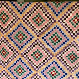May include: A colorful quilt with a repeating diamond pattern. The quilt features squares of pink, green, red, brown, purple, blue, and yellow. The design creates a geometric pattern, perfect for a bedspread or decorative throw.
