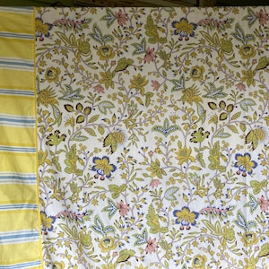 May include: A white fabric with a yellow and blue striped border. The fabric features a floral pattern with yellow, green, and pink flowers.