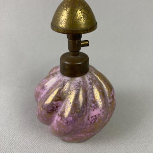 May include: A vintage perfume bottle with a pink and gold design. The bottle has a bulbous shape with a textured surface and a gold-colored metal top. The bottle's design features a pink base with gold accents.