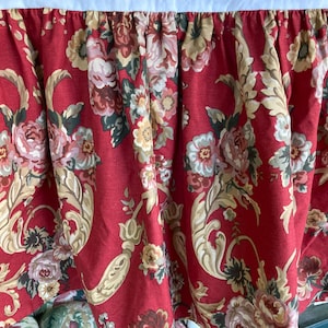 May include: Red bed skirt with a floral pattern featuring large roses and intricate gold scrollwork. The fabric has a textured linen look.