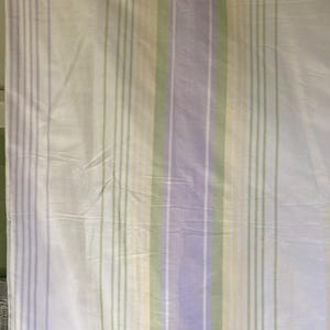 May include: White fabric with vertical stripes in shades of lavender, green, and yellow. The stripes are evenly spaced and run the length of the fabric. The fabric appears to be lightweight and possibly a sheet or curtain.