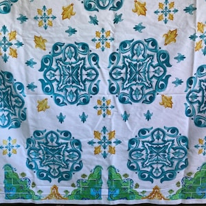 May include: White fabric with a repeating pattern of teal and yellow floral and geometric designs. The pattern includes large teal medallions, yellow leaf shapes, and smaller teal and yellow accents. The fabric has a slightly wrinkled texture.