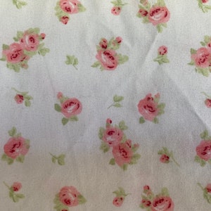 May include: White fabric with a repeating pattern of small pink roses. The roses are scattered randomly across the fabric.