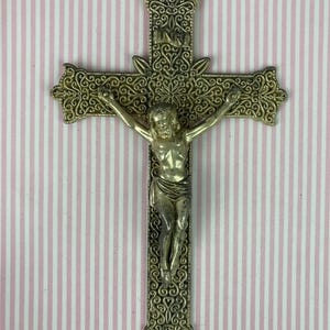 Op de afbeelding: Een metalen crucifix met een versierd kruis in filigraanstijl met ingewikkelde krulpatronen. Een figuur van Jezus is in het midden van het kruis geplaatst, met de letters INRI gegraveerd op een klein plaatje boven het hoofd van de figuur.