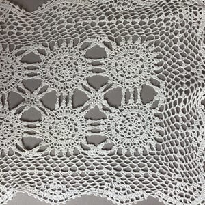 May include: White crocheted doily with a delicate floral pattern. The doily has a scalloped edge and is made of fine thread.