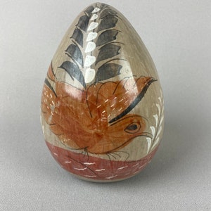 May include: A ceramic egg-shaped vase with a painted design of a bird in flight, surrounded by stylized leaves and flowers. The vase is painted in shades of brown, red, black, and white.