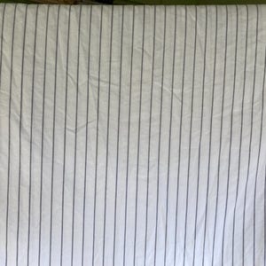 May include: White fabric with vertical gray stripes. The stripes are evenly spaced and run the length of the fabric. The fabric appears to be slightly wrinkled, suggesting it may be a sheet or other bedding item.