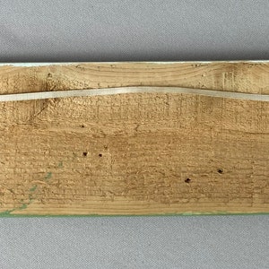 May include: A wooden sign with a light green painted border and a natural wood finish. The sign has a white string attached to the top for hanging.