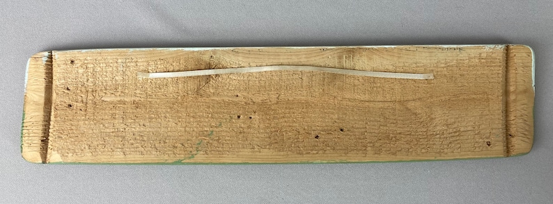 May include: A wooden sign with a light green painted border and a natural wood finish. The sign has a white string attached to the top for hanging.