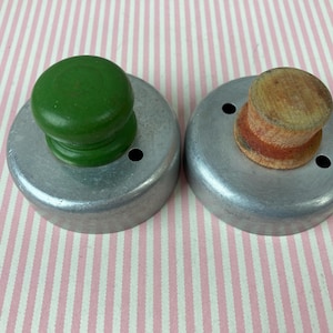 May include: Two metal cookie cutters with wooden handles. The cutter on the left has a green handle and the cutter on the right has a brown handle.