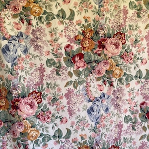 May include: A fabric featuring a dense floral pattern on a white background. The design includes clusters of pink, red, and yellow roses, purple lilac sprigs, and small pink blossoms, interspersed with light blue ribbons and green foliage.
