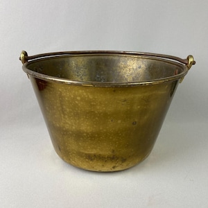 May include: A vintage brass bucket with a wire handle. The bucket has a worn, aged patina and is perfect for a rustic or farmhouse decor.