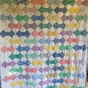 May include: A white quilt with a pattern of colorful bowties. The bowties are made of different fabrics with floral and checkered patterns. The quilt is quilted with a diamond pattern.