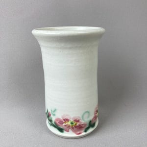 May include: White ceramic vase with a floral design. The vase has a wide mouth and a narrow base. The floral design is in shades of pink and green.