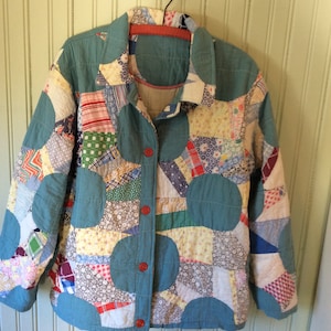 May include: A teal blue quilted jacket with a button closure. The jacket is made of patchwork fabric in various colors and patterns, including red, white, blue, green, and yellow.
