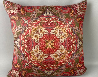 May include: Square decorative pillow with a detailed, symmetrical pattern. The design features a mix of red, yellow, and cream colors on a green background. The pillow has a soft, inviting appearance.