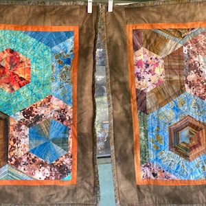 May include: Two fabric panels with hexagon patterns. Each panel features a brown border with an orange inner border. The hexagon designs incorporate shades of blue, teal, brown, and red, creating a colorful, abstract quilt design.