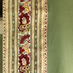 May include: A section of fabric featuring a central floral pattern with burgundy, yellow, and peach flowers on a white background. The design is flanked by vertical stripes with a cream background and green accents. The right side is solid green.
