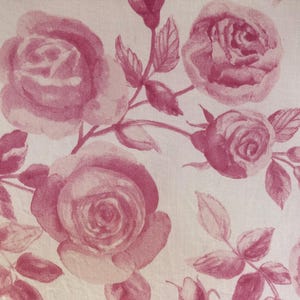 May include: A pink floral fabric with a repeating pattern of roses and leaves. The fabric has a soft, delicate look and feel.