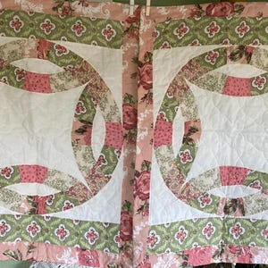May include: Two vintage-style quilts with a double wedding ring pattern. The quilts feature a white center, surrounded by rings of floral fabric in pink, green, and cream. The borders have a pink rose pattern.