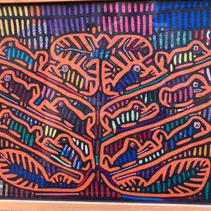 May include: A framed, colorful artwork featuring an orange tree-like design with stylized figures. The figures are filled with various colors, including blue, green, and yellow. The background is a mix of vertical lines in multiple colors. The frame is made of light-colored wood.