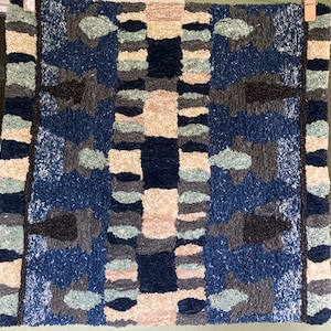 May include: A blue, beige, and gray patterned rug with a geometric design. The rug has a textured, woven look.