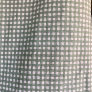 May include: Close-up of a fabric with a repeating pattern of small white squares on a sage green background. The fabric has a slightly textured appearance, with the squares arranged in a grid-like formation. The overall aesthetic is simple and classic.